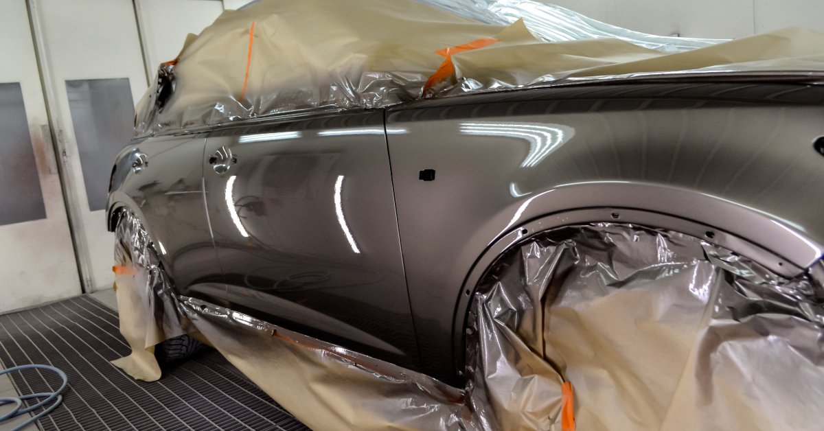 A car is in a bay and it has all the glass and tires covered with a protective tarp. The car is gray.