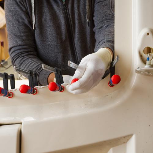 A man wearing white gloves places and tightens many clamps on a car window frame as part of an adhesive repair.